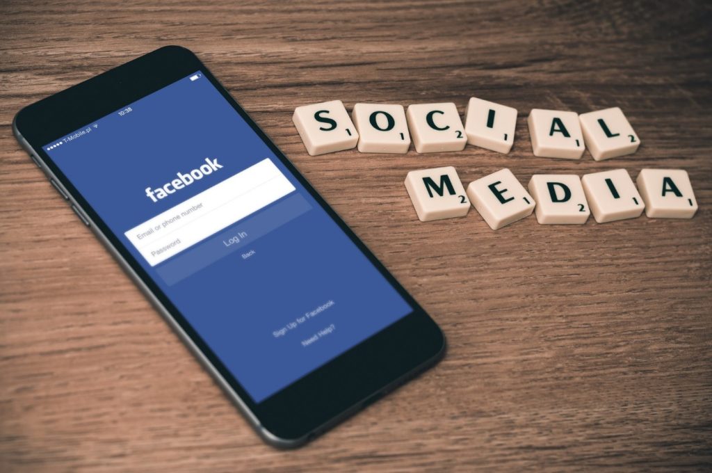An iPhone with the Facebook app open next to some scrabble tiles that spell out "social media"