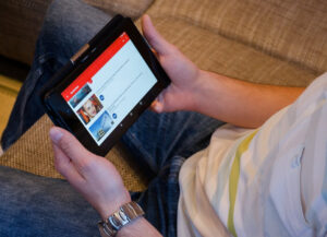 A man holding a tablet with YouTube opened on it.