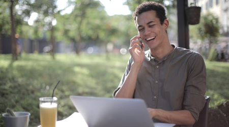 An image of a cheerful man talking on the phone while sitting outdoors