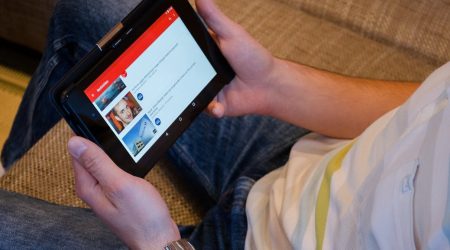A man holding a tablet with YouTube opened on it.